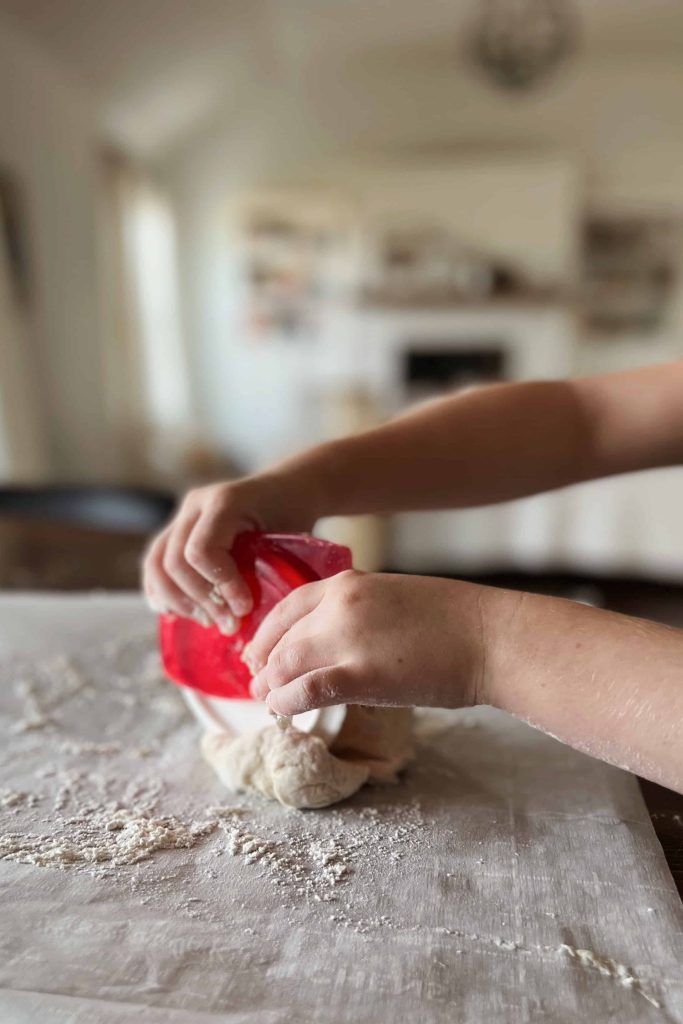 A child cuts bannock bread dough with a kid-safe pizza cutter. 
