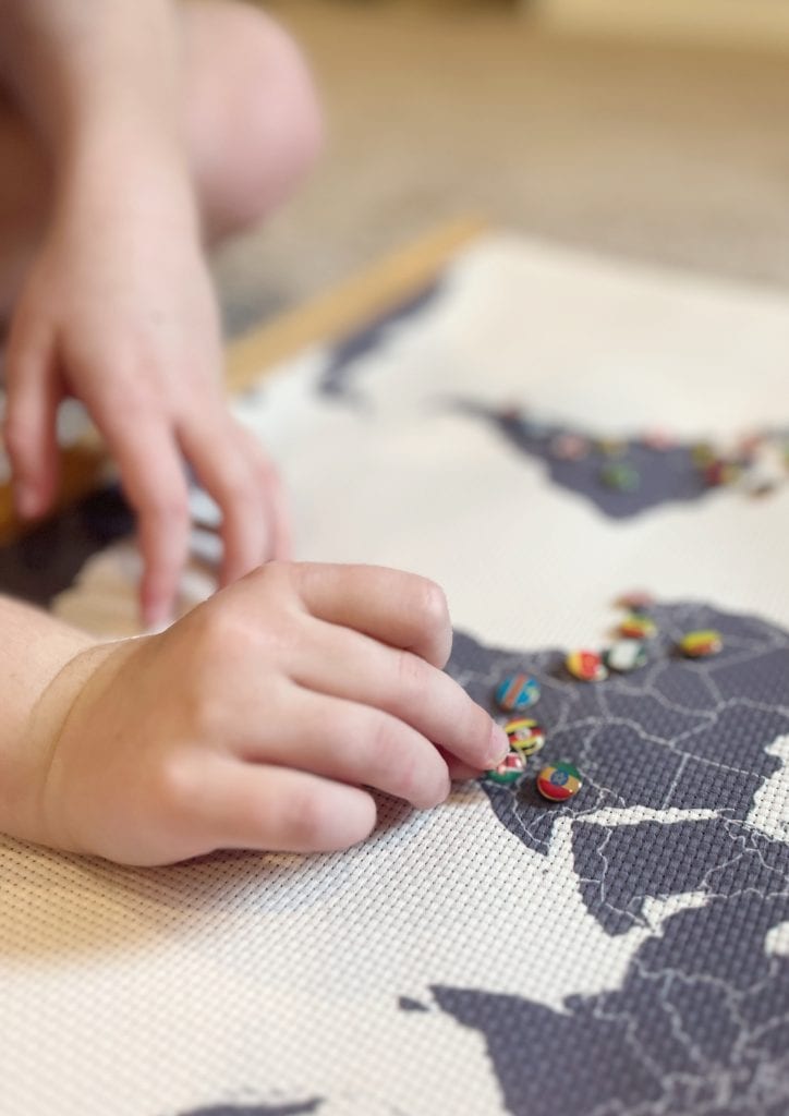 A child places flag pins onto a cross stitch world map after she completes a new unit study from the Global Explorers Club.